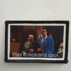 Puede incluir: Un parche bordado en blanco y negro con una foto de dos hombres con traje. El texto "Play it nice and cool" está impreso debajo de la foto.