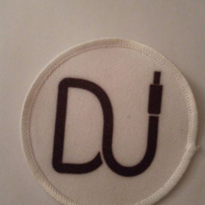 May include: White round patch with a brown "DU" logo. The "D" is a stylised letter and the "U" is a stylised cable connector.