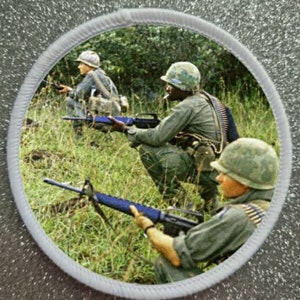 Op de afbeelding: Drie soldaten in camouflage-uniformen houden geweren vast in een jungle-omgeving. De soldaten dragen helmen en munitie-gordels. De afbeelding is een vintage foto.