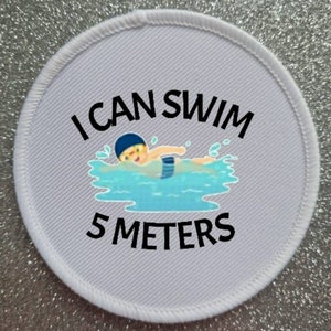 May include: White round patch with black text that reads "I can swim 5 meters". A cartoon illustration of a person swimming in blue water is in the center of the patch.