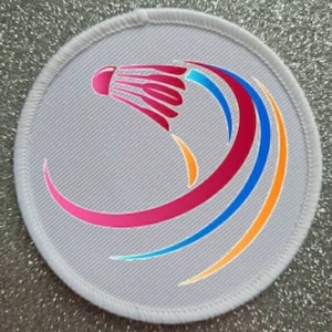 May include: White round patch with a colorful badminton shuttlecock design. The shuttlecock is pink, blue, and orange. The design is on a white background.