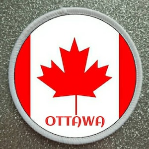 Puede incluir: Un parche circular blanco, rojo y blanco con una hoja de arce roja y la palabra "OTTAWA" en letras rojas.