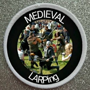 May include: A black and white circular patch with the text "MEDIEVAL LARPING" in white. The patch features a scene of people in medieval costumes fighting with swords and shields.