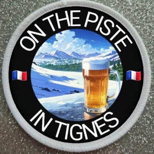 May include: A round white patch with black text that reads "On the piste in Tignes". The patch features a mountain scene with a glass of beer in the foreground. The French flag is on either side of the text.