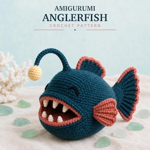 May include: A dark teal crocheted amigurumi anglerfish with a light yellow lure, coral-colored fins, and a wide mouth containing white teeth. The text AMIGURUMI ANGLERFISH CROCHET PATTERN is displayed at the top of the image in dark blue letters.