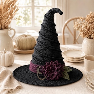May include: A black crocheted witch hat featuring a spiraling texture, a wide brim, and a dark purple band. The band is decorated with a large dark purple crocheted flower, two green crocheted leaves, and a gold-toned crescent moon charm with a chain.