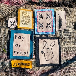 Puede incluir: Colección de parches de tela hechos a mano con varios diseños. Incluye parches con ilustraciones de insectos, una cabeza de ciervo, una espiral abstracta y el texto "Pay an artist". Los parches son de varios colores y tamaños.