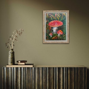 May include: Framed painting of red and white mushrooms in a green forest setting.