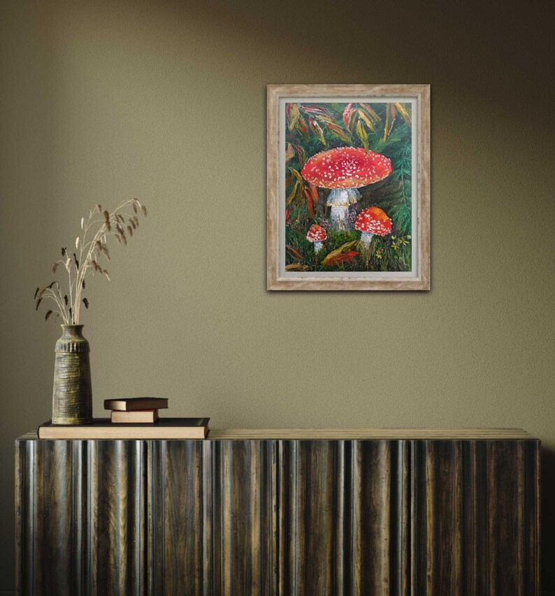 May include: Framed painting of red and white mushrooms in a green forest setting.