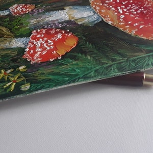 May include: A close-up of a painting of red and white mushrooms in a green forest setting. The mushrooms have white spots and are painted in a realistic style.