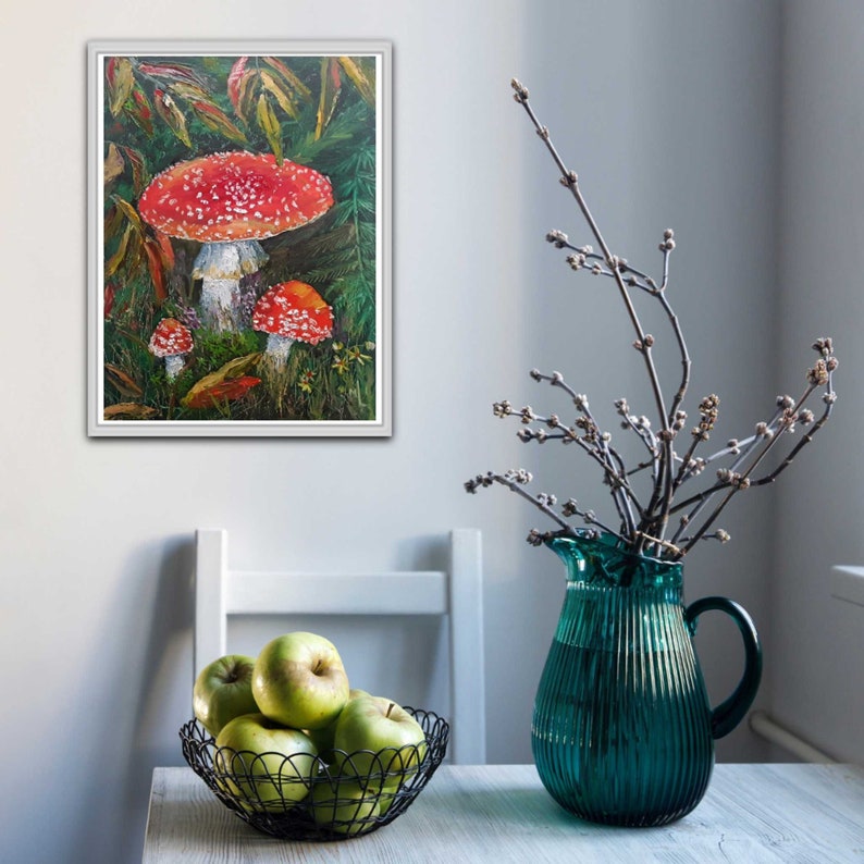 May include: A framed painting of three red and white mushrooms with white spots in a forest setting. The mushrooms are surrounded by green leaves and brown branches.