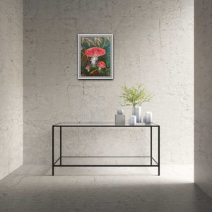 May include: A framed painting of red and white mushrooms in a green forest setting.