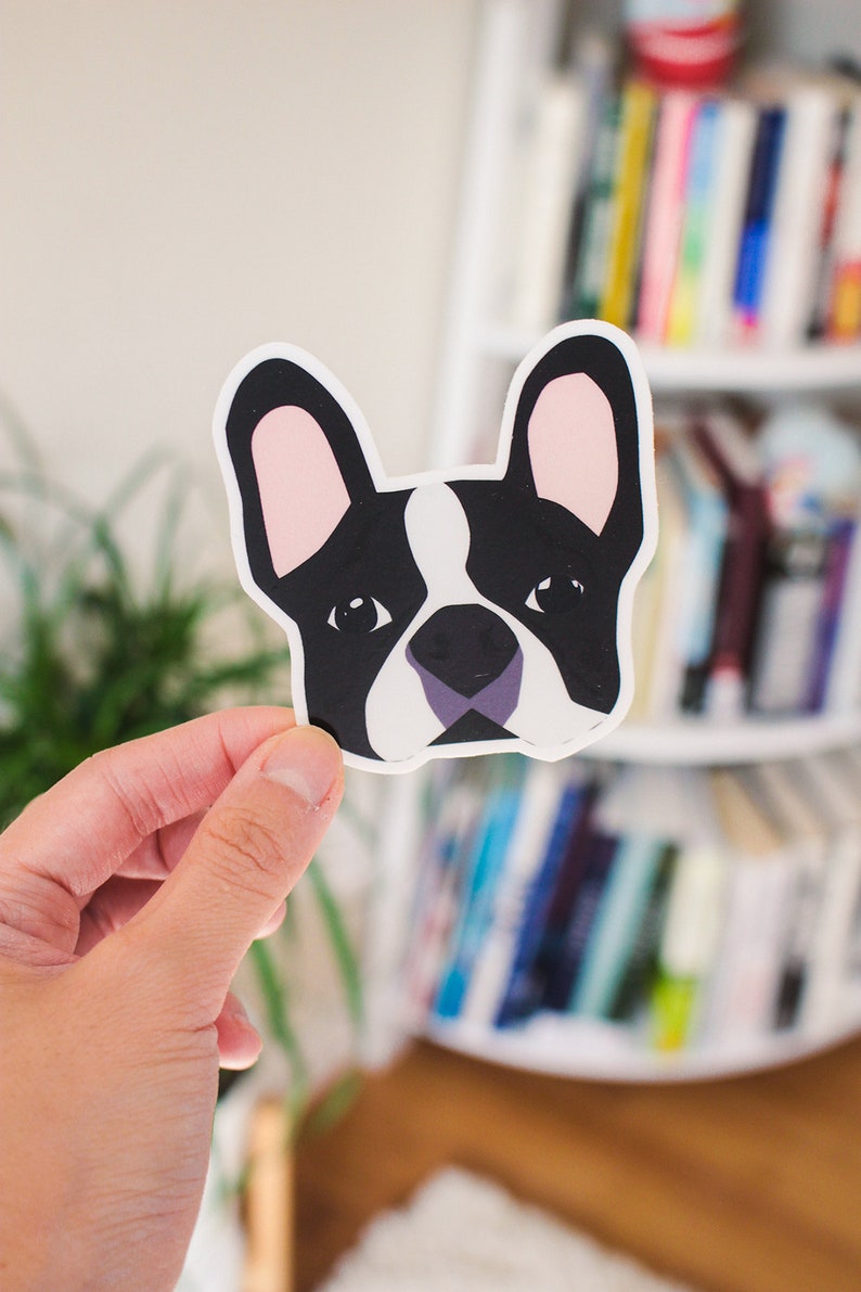 May include: A black and white illustrated sticker of a French bulldog's face. The sticker has a white background and pink ears.