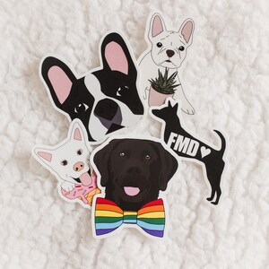 May include: Five dog stickers, each with a different design. One sticker features a black and white French bulldog with pink ears, another features a white French bulldog with a plant in a pot, another features a black Labrador Retriever wearing a rainbow bow tie, another features a white dog with a pink donut, and the last sticker features a black silhouette of a dog with the text "FMD" and a heart.