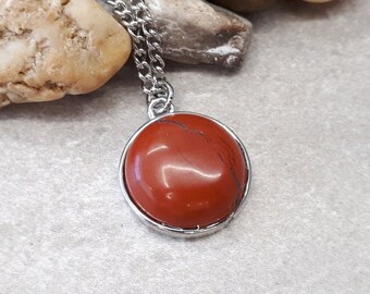 Op de afbeelding: Een zilveren ketting met een ronde hanger van rode edelsteen.
