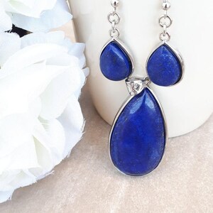 Pu&ograve; includere: Orecchini pendenti color argento con tre pietre di lapislazzuli blu intenso a forma di goccia. La pietra pi&ugrave; grande &egrave; in basso, con due pietre pi&ugrave; piccole sopra. Sfondo bianco.