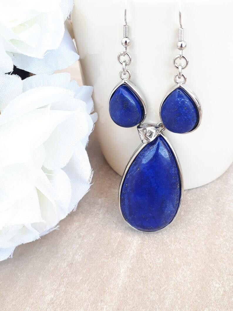 Pu&ograve; includere: Orecchini pendenti color argento con tre pietre di lapislazzuli blu intenso a forma di goccia. La pietra pi&ugrave; grande &egrave; in basso, con due pietre pi&ugrave; piccole sopra. Sfondo bianco.