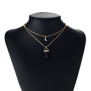 Può includere: Una collana dorata a due strati con un ciondolo di cristallo nero e un ciondolo a forma di mezzaluna.