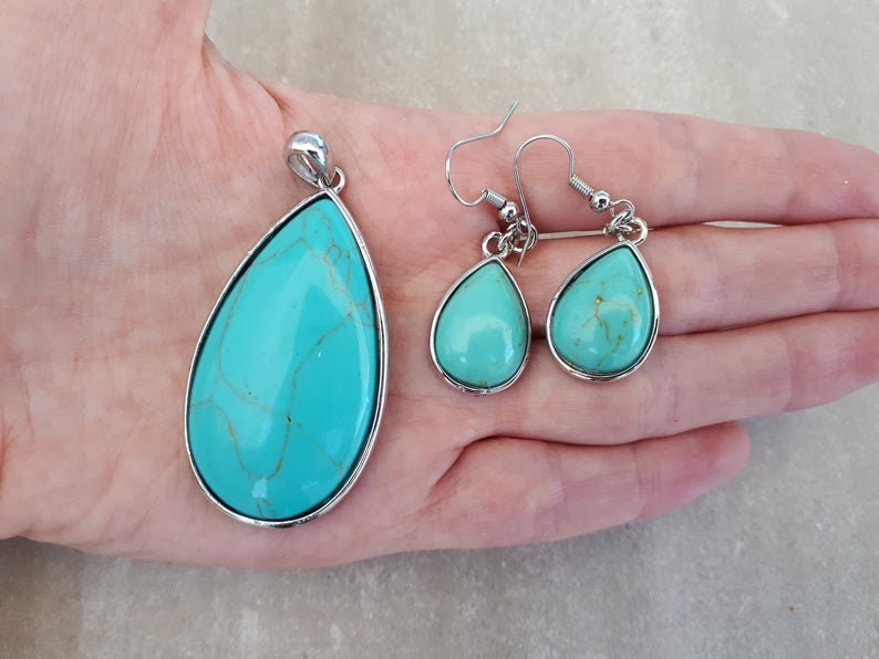 Puede incluir: Un conjunto de joyas turquesas con un colgante y pendientes a juego. Las piedras en forma de l&aacute;grima tienen un borde de metal plateado. El colgante es m&aacute;s grande que los pendientes. Las piedras turquesas tienen vetas marrones.