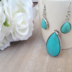 Puede incluir: Un conjunto de joyas turquesas con un colgante y pendientes a juego. Las piedras en forma de l&aacute;grima est&aacute;n engastadas en metal plateado. Los pendientes tienen cierre de gancho. Flores blancas en el fondo.