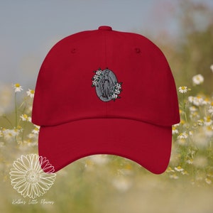 Puede incluir: Gorra de béisbol roja con una imagen bordada de la Virgen María con flores blancas.
