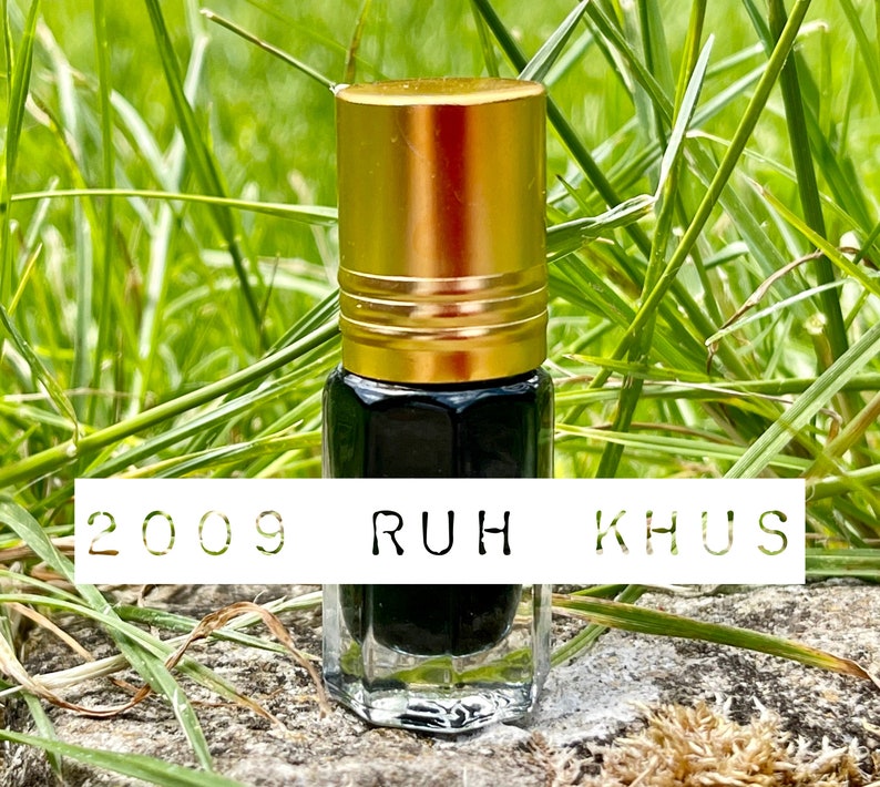 May include: A small, clear glass bottle with a black liquid inside. The bottle has a gold cap and is labeled "2009 RUH KHUS".