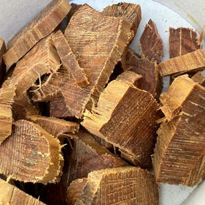Könnte beinhalten: Nahaufnahme einer Sammlung unregelmäßig geformter, hellbrauner Holzstücke. Das Holz hat eine raue, strukturierte Oberfläche mit sichtbaren Maserungsmustern. Die Stücke befinden sich in einem weißen Behälter, was auf ein Naturprodukt hindeutet.