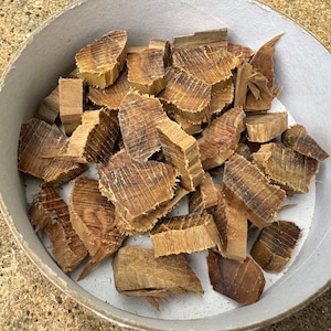 May include: A white bowl filled with brown wood chips. The chips are of various sizes and shapes, and some have a darker brown colour.