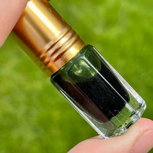 May include: A small glass bottle with a gold cap, filled with a dark green liquid. The bottle is being held by a hand.