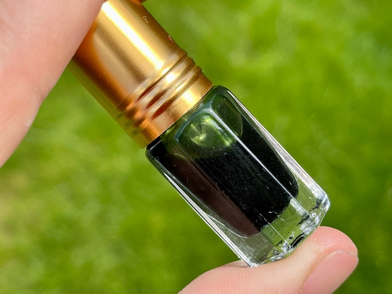 May include: A small glass bottle with a gold cap, filled with a dark green liquid. The bottle is being held by a hand.
