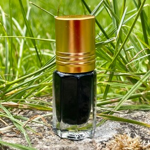 May include: A small, clear glass bottle with a gold cap. The bottle is filled with a dark liquid and is sitting on a rock.