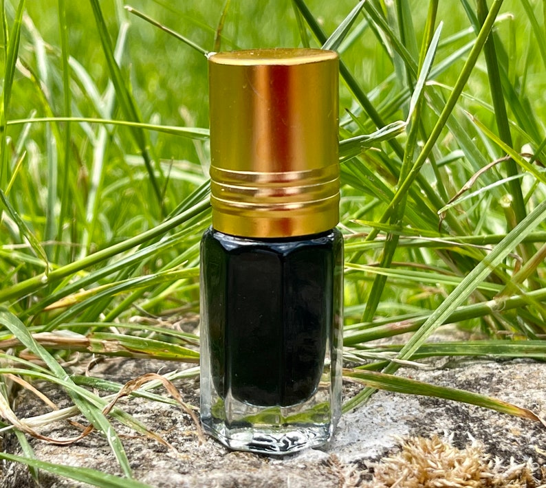 May include: A small, clear glass bottle with a gold cap. The bottle is filled with a dark liquid and is sitting on a rock.