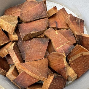 Könnte beinhalten: Eine Schüssel gefüllt mit kleinen, unregelmäßig geformten Stücken rotbraunen Holzes. Das Holz hat eine grobe Textur und scheint getrocknet zu sein.