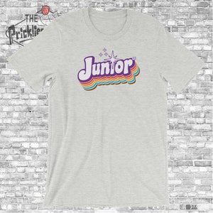 May include: A heather grey t-shirt with a retro-style graphic of the word "Junior" in rainbow colors with a starburst above it.