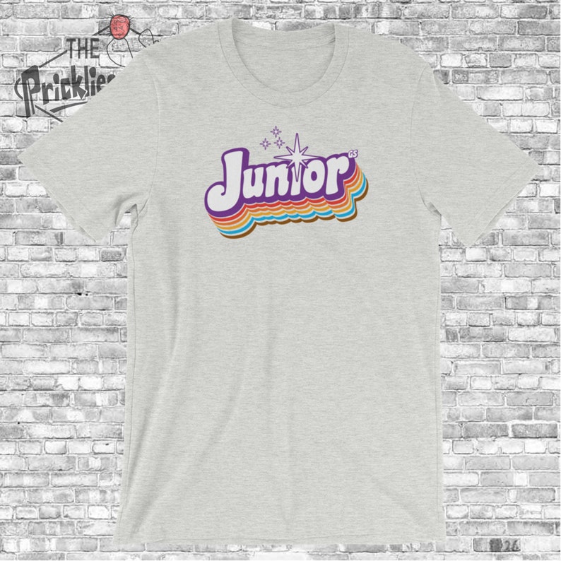 May include: A heather grey t-shirt with a retro-style graphic of the word "Junior" in rainbow colors with a starburst above it.