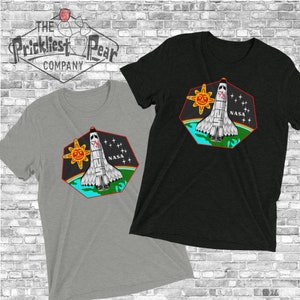 May include: Two t-shirts with a graphic of a space shuttle launching into space with a sun and stars in the background. The text "NASA" is on the graphic. The t-shirts are grey and black.