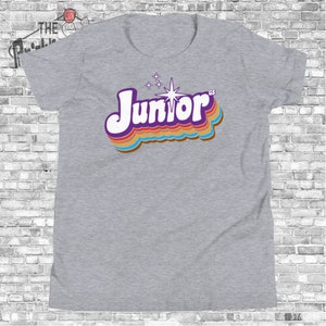 May include: Gray t-shirt with a retro-style graphic of the word "Junior" in rainbow colors with a starburst above it.