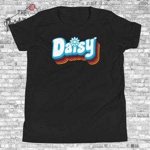 May include: Black t-shirt with a retro-style graphic of the word "Daisy" in white with a blue daisy flower in the center. The word is outlined in rainbow colors.