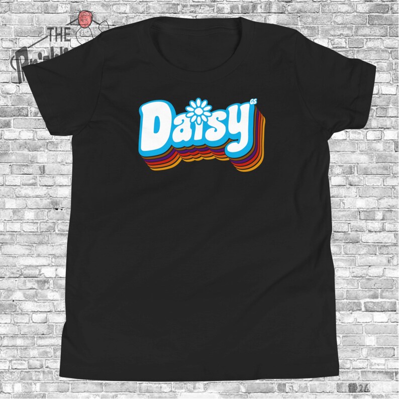 May include: Black t-shirt with a retro-style graphic of the word "Daisy" in white with a blue daisy flower in the center. The word is outlined in rainbow colors.