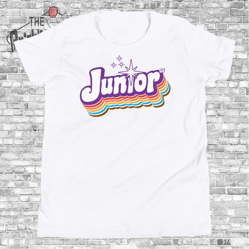 May include: White t-shirt with a purple, rainbow, and white retro-style graphic that says "Junior" with a star and four small stars above the word.