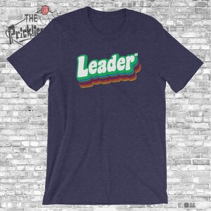 May include: A navy blue t-shirt with a retro-style graphic that says "Leader" in green, orange, red, and white.