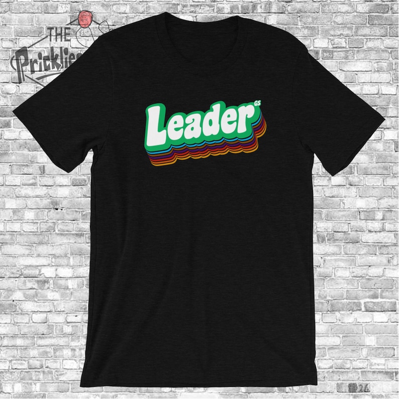 May include: Black t-shirt with a green, rainbow-colored "Leader" graphic.