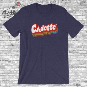 K&ouml;nnte beinhalten: Ein marineblaues T-Shirt mit einer Retro-Grafik des Wortes "Cadette" mit einem Zelt-Symbol und den Buchstaben "GS" in kleinerer Schrift.
