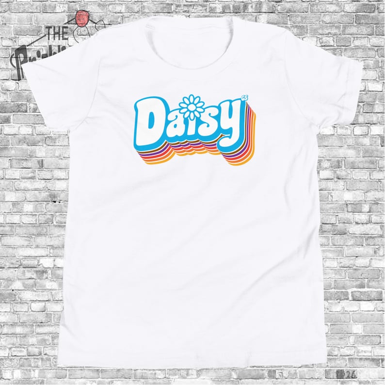 May include: White t-shirt with a retro-style graphic of the word "Daisy" in blue with a yellow daisy in the center. The word is outlined in rainbow colors.
