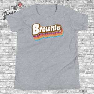 May include: Gray t-shirt with a retro-style graphic of the word "Brownie" in brown with rainbow stripes.