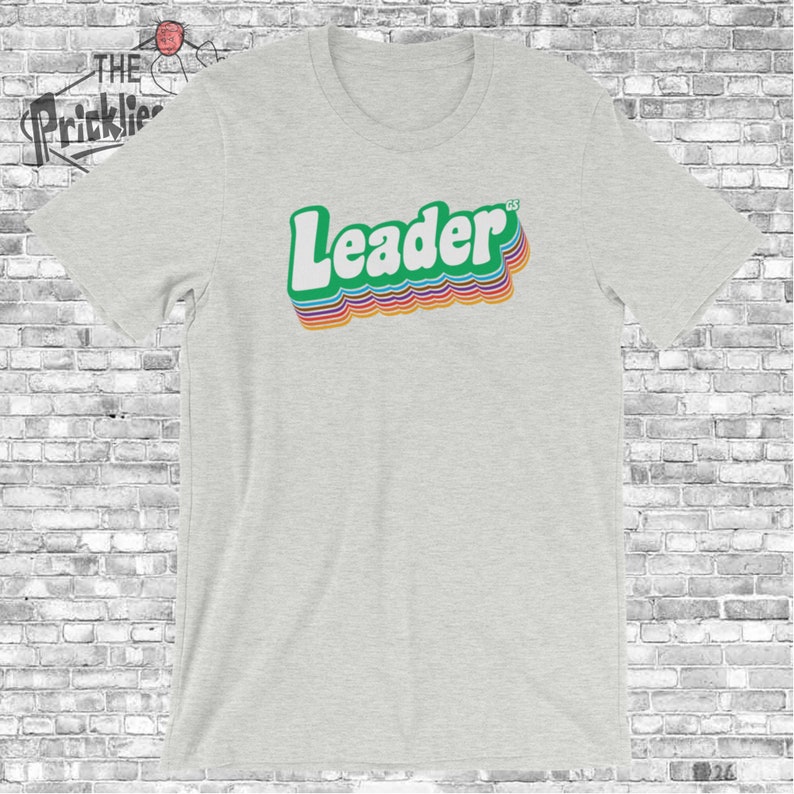 May include: A heather grey t-shirt with a retro-style graphic of the word "Leader" in rainbow colors.