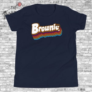 May include: A navy blue t-shirt with a retro-style graphic of the word "Brownie" in rainbow colors. The graphic also includes a basketball.