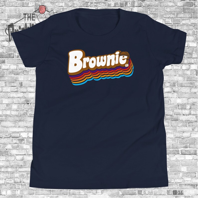 May include: A navy blue t-shirt with a retro-style graphic of the word "Brownie" in rainbow colors. The graphic also includes a basketball.