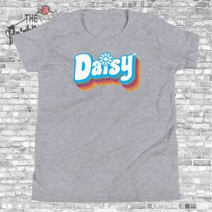 May include: A gray t-shirt with a retro-style graphic of the word "Daisy" in blue with a white daisy in the center. The word is surrounded by rainbow-colored stripes.