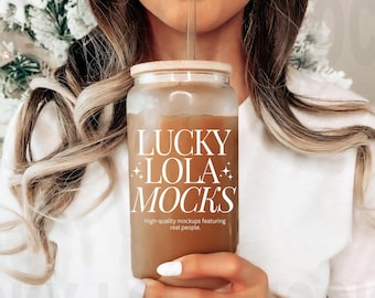 Puede incluir: Una mujer sostiene un vaso de vidrio transparente con un líquido marrón y una pajita. El vaso tiene el texto "LUCKY LOLA MOCKS" y "High-quality mockups featuring real people." impreso en él.
